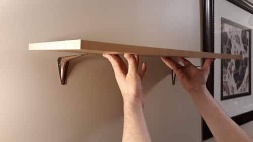 Two hands putting up a shelf on the wall.
